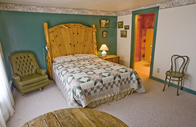 A second queen room with attached bathroom and comfortable green chair. 